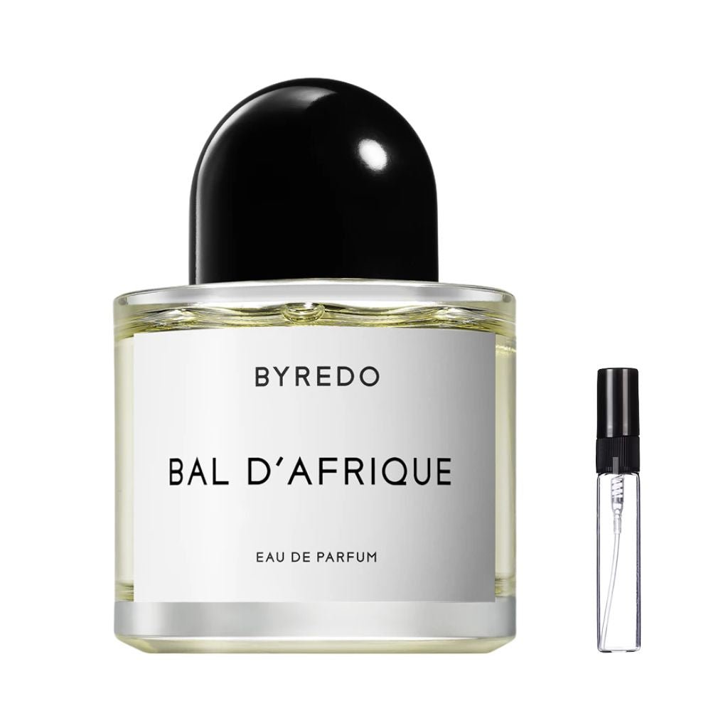 Przezroczysty, cylindryczny flakon perfum Byredo Bal d'Afrique z białą kwadratową etykietą, czarnymi napisami oraz charakterystycznym czarnym, półokrągłym korkiem, obok którego znajduje się szklana fiolka odlewki – ODVARO.