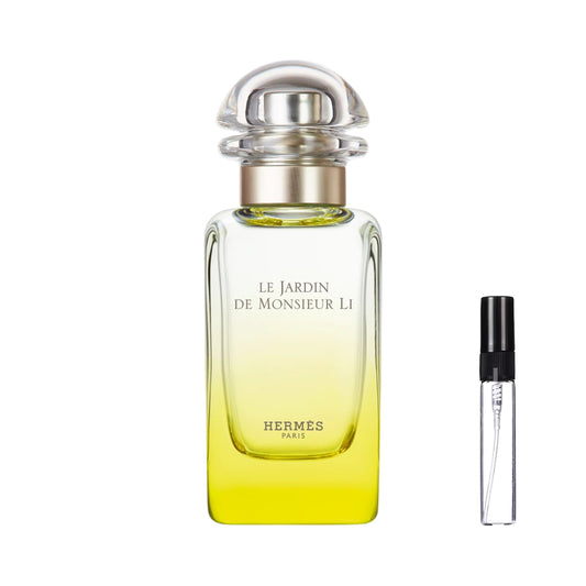 Smukły, prostokątny flakon perfum Hermès Le Jardin de Monsieur Li o gradientowym, żółto-zielonym szkle z minimalistycznymi, czarnymi napisami i przezroczystym, półokrągłym korkiem, obok którego zaprezentowana jest szklana fiolka odlewki – ODVARO.