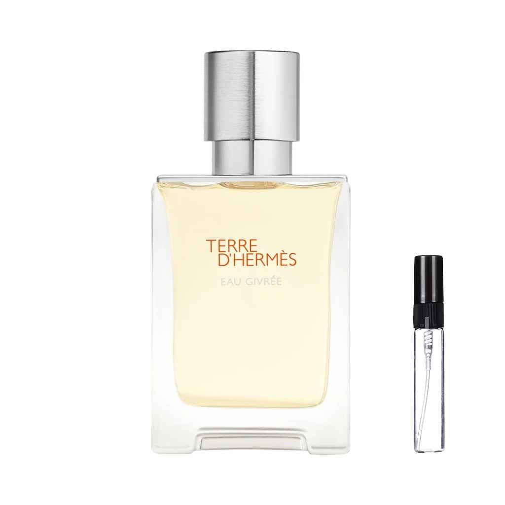 Kwadratowy, masywny flakon perfum Terre d'Hermès Eau Givree z jasnożółtym płynem, pomarańczowymi napisami oraz cylindrycznym, srebrnym korkiem o szczotkowanej fakturze, obok którego zaprezentowana jest szklana fiolka odlewki – ODVARO.