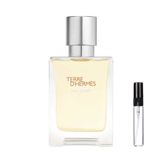 Kwadratowy, masywny flakon perfum Terre d'Hermès Eau Givree z jasnożółtym płynem, pomarańczowymi napisami oraz cylindrycznym, srebrnym korkiem o szczotkowanej fakturze, obok którego zaprezentowana jest szklana fiolka odlewki – ODVARO.