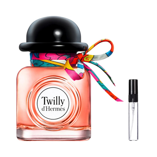 Kwadratowy flakon perfum Twilly d'Hermès z brzoskwiniowym płynem, białym okrągłym logo, czarnym korkiem w kształcie melonika i kolorową jedwabną wstążką, oraz szklana fiolka odlewki – ODVARO.