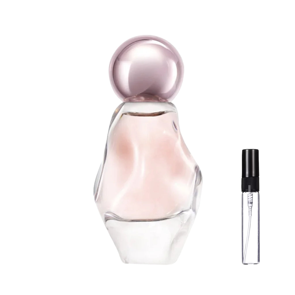 Asymetryczny, przezroczysty flakon perfum Cosmic o rzeźbionym kształcie, z jasnoróżowym płynem i okrągłym, metalicznym korkiem oraz szklana fiolka odlewki – ODVARO.