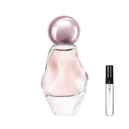 Asymetryczny, przezroczysty flakon perfum Cosmic o rzeźbionym kształcie, z jasnoróżowym płynem i okrągłym, metalicznym korkiem oraz szklana fiolka odlewki – ODVARO.