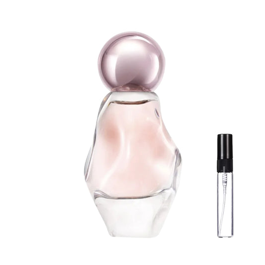 Asymetryczny, przezroczysty flakon perfum Cosmic o rzeźbionym kształcie, z jasnoróżowym płynem i okrągłym, metalicznym korkiem oraz szklana fiolka odlewki – ODVARO.