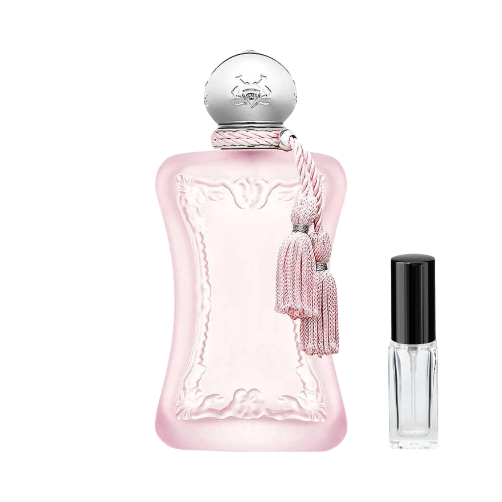 Matowy, jasnoróżowy flakon damskich perfum Delina La Rosée Parfums de Marly z rzeźbionymi ornamentami, srebrnym okrągłym korkiem i różowymi chwostami, a obok niego szklana fiolka odlewki – ODVARO.