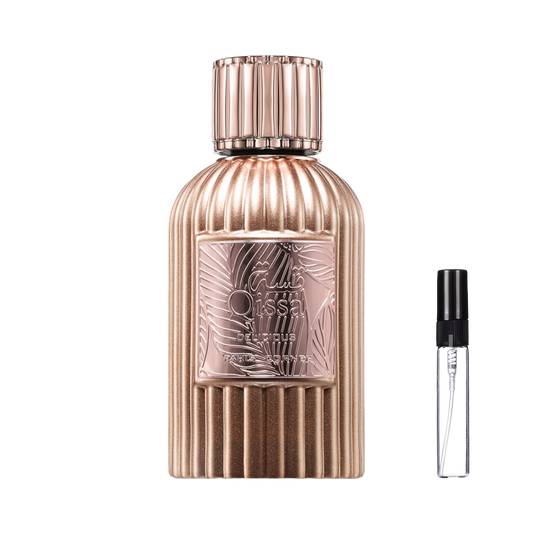 Miedziano-złoty, żebrowany flakon Paris Corner Qissa Delicious z ozdobną etykietą w motywy roślinne i pasującym korkiem obok szklanej fiolki odlewki – ODVARO