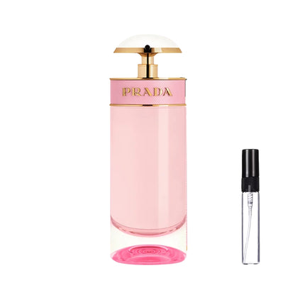 Wysoki, cylindryczny flakon perfum Prada Candy Florale z jasnoróżowym płynem, różową opaską ze złotym logo i złotym dozownikiem w kształcie parasolki, oraz szklana fiolka odlewki – ODVARO.